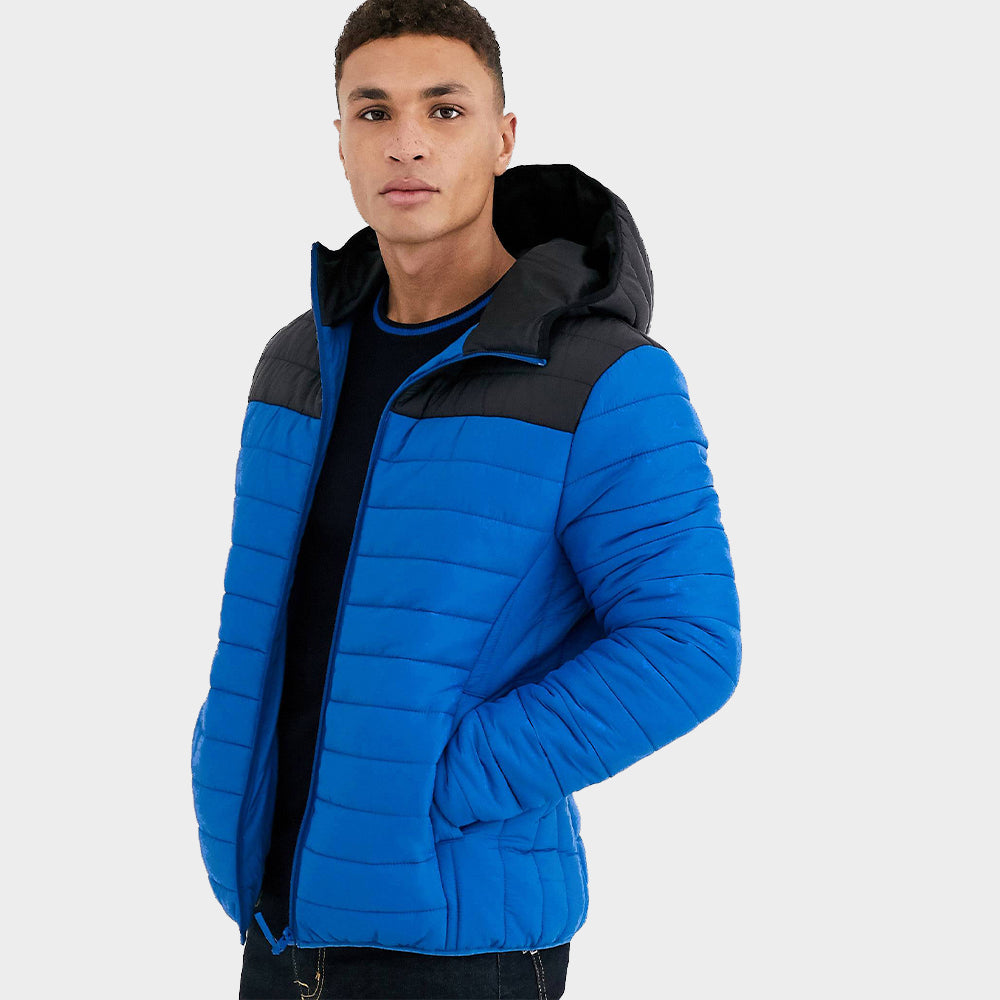 A man is standing wearing a blue quilted puffer jacket with his hands in the slash pockets